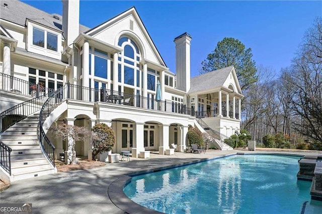 back of house featuring a balcony, a patio, an outdoor pool, a chimney, and stairs