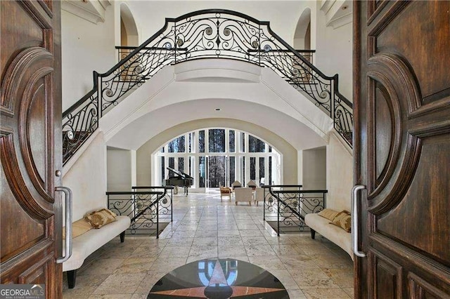 foyer entrance featuring stairway, arched walkways, and a towering ceiling