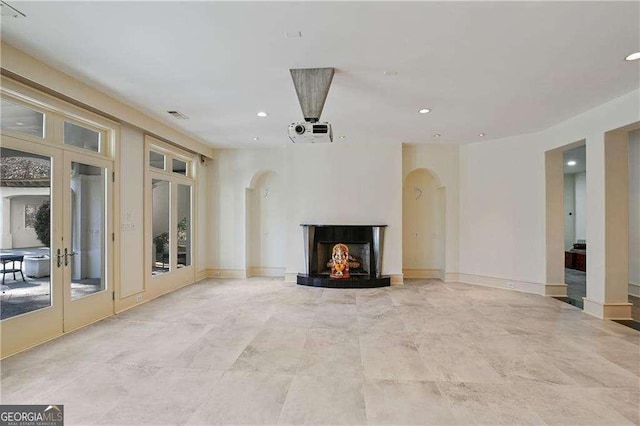 unfurnished living room with arched walkways, french doors, recessed lighting, baseboards, and a lit fireplace