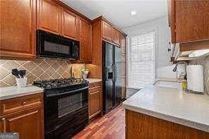 kitchen with light countertops, decorative backsplash, brown cabinets, black appliances, and a sink