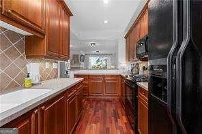 kitchen featuring brown cabinets, black appliances, backsplash, dark wood-style floors, and light countertops