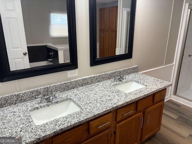 bathroom featuring double vanity, a decorative wall, wood finished floors, and a sink