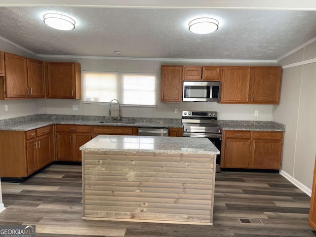 kitchen with dark wood-type flooring, a sink, stainless steel appliances, brown cabinetry, and crown molding