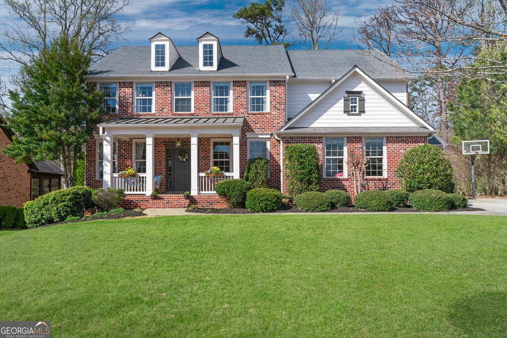 colonial-style house with a front yard, covered porch, and brick siding