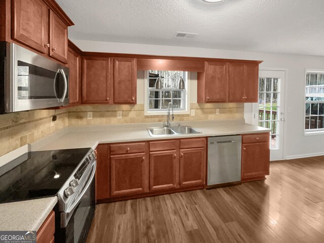 kitchen with visible vents, decorative backsplash, light wood-style flooring, stainless steel appliances, and a sink