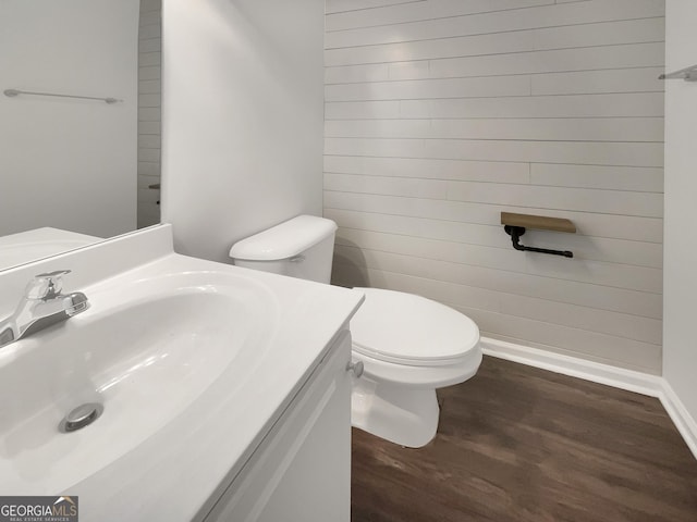 half bathroom featuring wood walls, toilet, vanity, and wood finished floors
