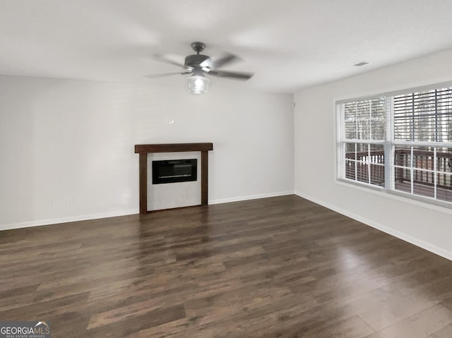 unfurnished living room with a glass covered fireplace, baseboards, ceiling fan, and dark wood-style flooring