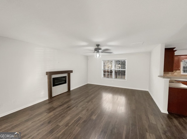 unfurnished living room with a glass covered fireplace, baseboards, dark wood-style flooring, and ceiling fan