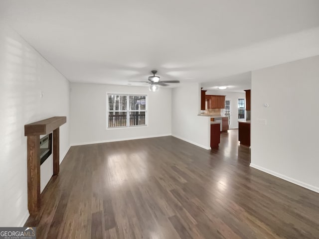 unfurnished living room featuring a glass covered fireplace, baseboards, dark wood-type flooring, and ceiling fan