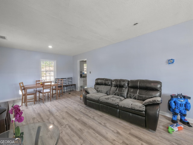 living room featuring visible vents, wood finished floors, baseboards, and a textured ceiling