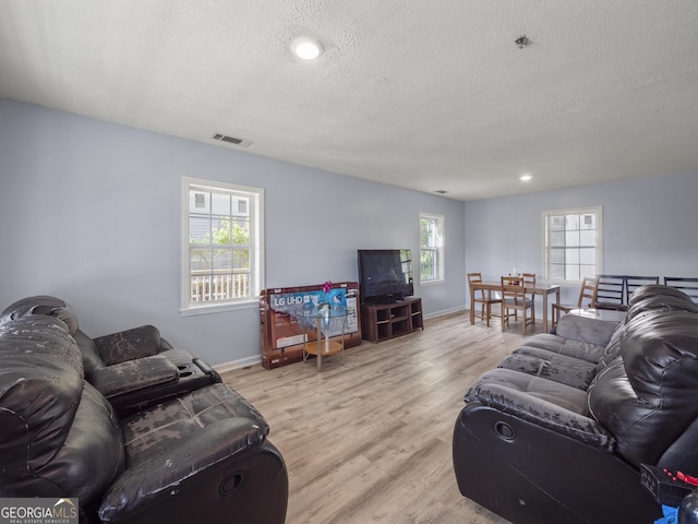 living room with visible vents, a textured ceiling, a healthy amount of sunlight, and light wood-style flooring