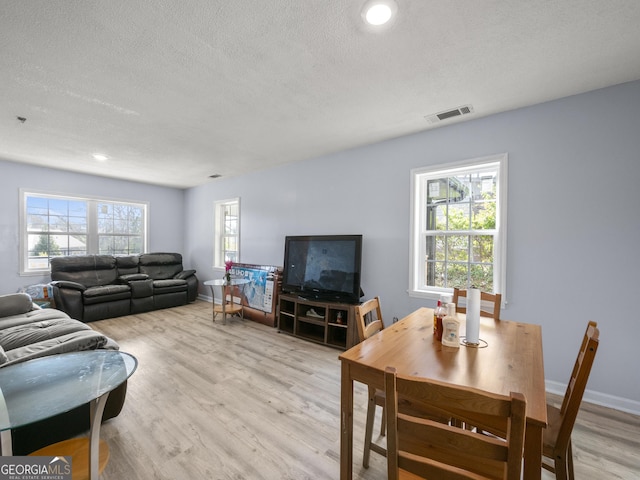 living room featuring light wood-type flooring, baseboards, a textured ceiling, and visible vents