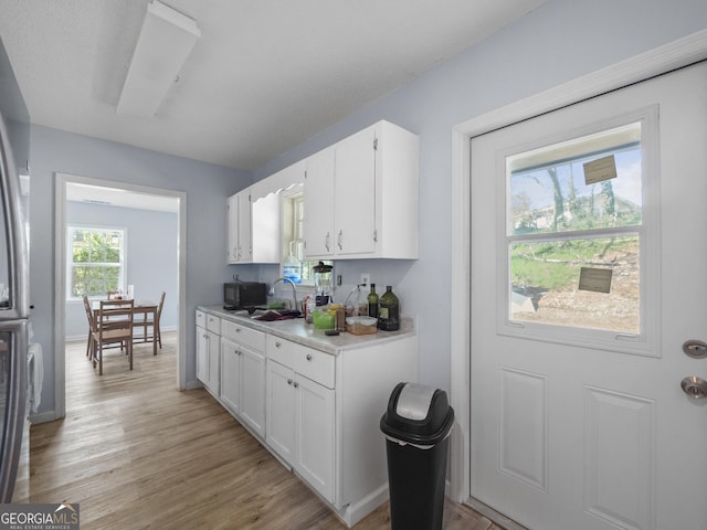 kitchen with baseboards, light wood finished floors, a sink, light countertops, and white cabinetry