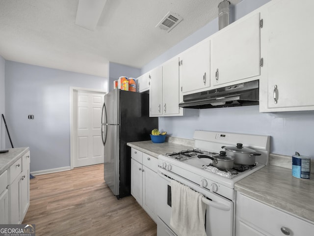 kitchen with visible vents, under cabinet range hood, white range with gas cooktop, freestanding refrigerator, and white cabinetry