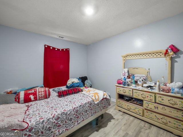 bedroom featuring visible vents, a textured ceiling, and wood finished floors