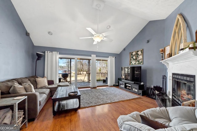 living room with high vaulted ceiling, a ceiling fan, a glass covered fireplace, and wood finished floors