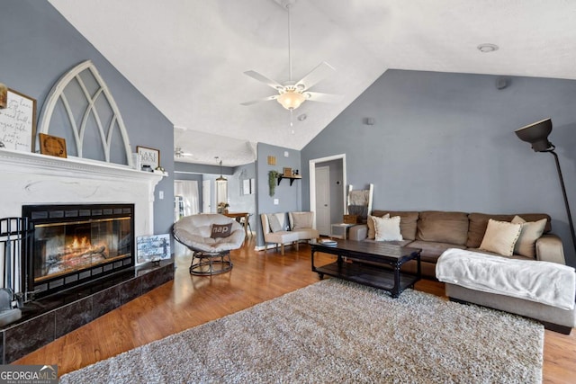 living room featuring high vaulted ceiling, a ceiling fan, a glass covered fireplace, and wood finished floors
