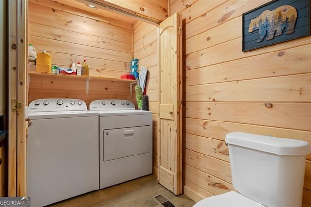 washroom featuring wooden walls, visible vents, washer and dryer, and light wood-style floors