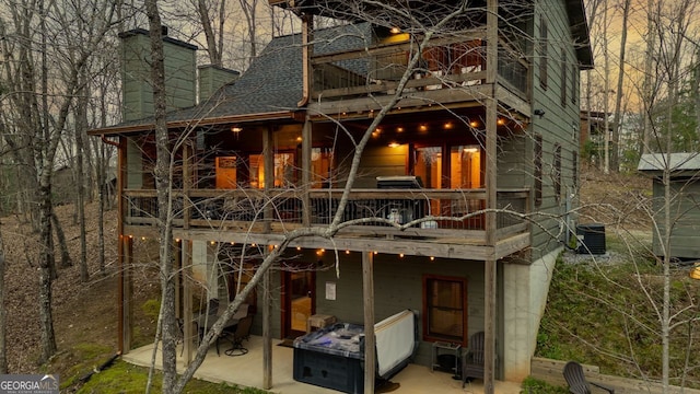 back of property with a patio area, a chimney, a shingled roof, and a balcony