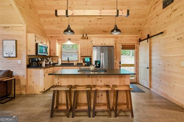kitchen featuring dark countertops, appliances with stainless steel finishes, light brown cabinetry, wood finished floors, and wood walls