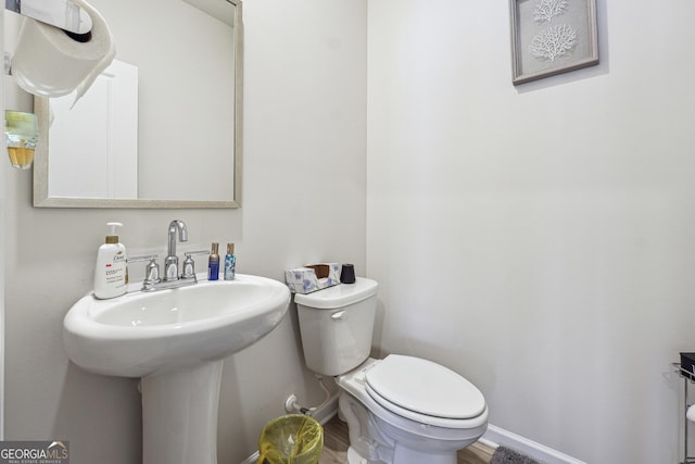 bathroom with toilet, wood finished floors, baseboards, and a sink