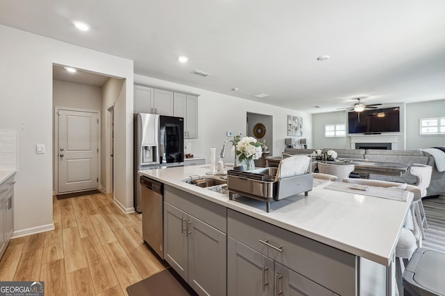 kitchen with light countertops, gray cabinets, stainless steel appliances, a ceiling fan, and a kitchen island with sink
