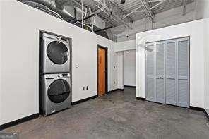 clothes washing area with a high ceiling, laundry area, stacked washer / dryer, and baseboards