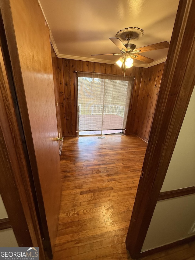 spare room with a ceiling fan, wood finished floors, crown molding, and wood walls