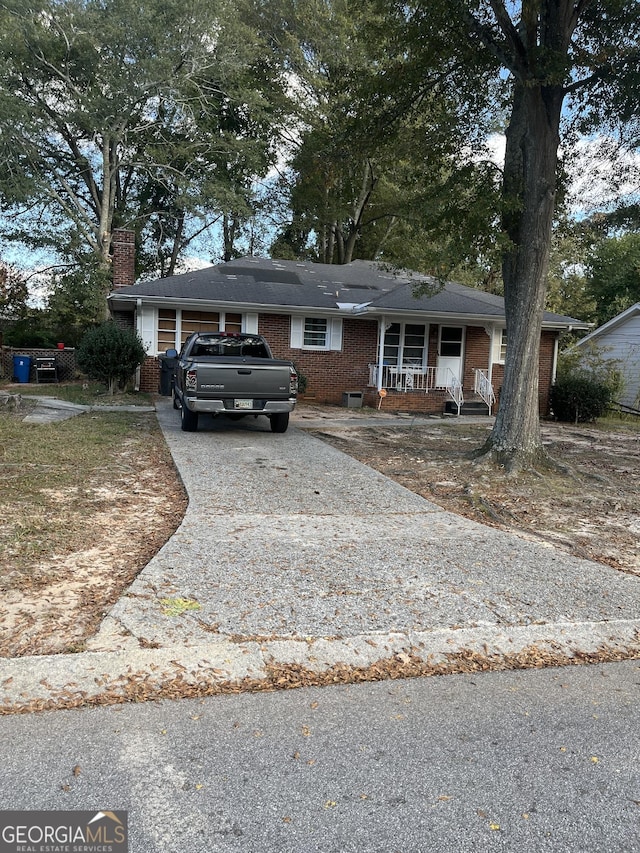 view of front facade featuring a chimney, brick siding, covered porch, and driveway