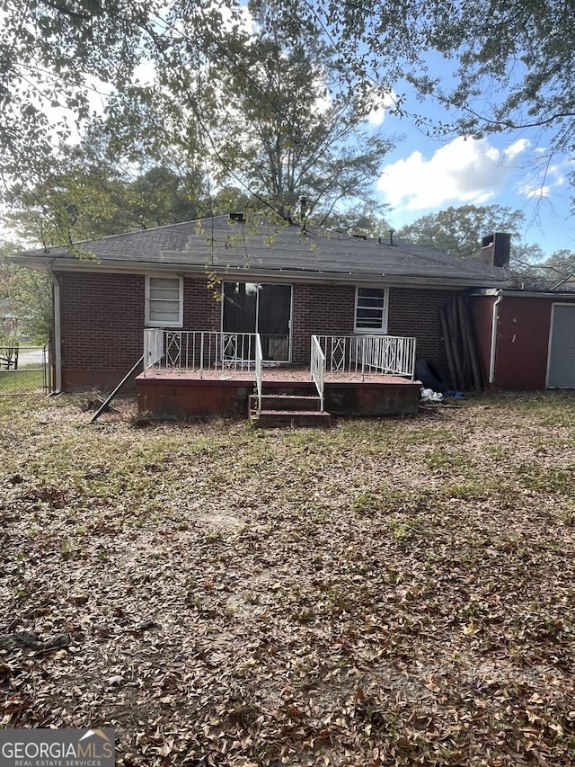 rear view of property with a deck, brick siding, and a chimney