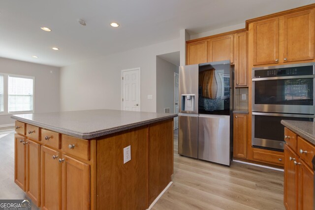 kitchen with a center island, brown cabinetry, light wood-type flooring, and stainless steel appliances