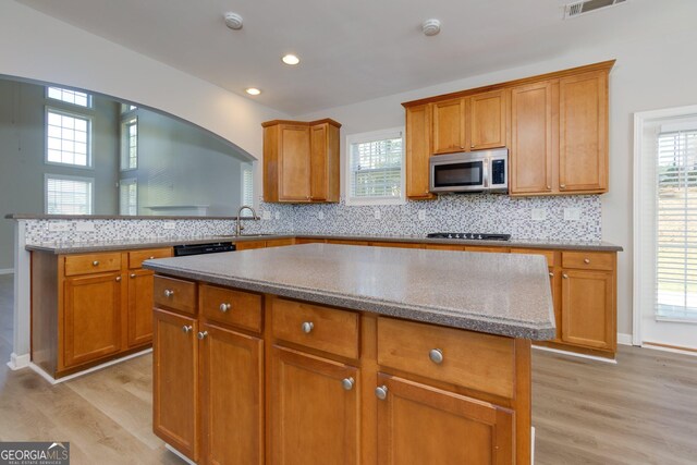 kitchen featuring a kitchen island, a peninsula, light wood-style flooring, decorative backsplash, and appliances with stainless steel finishes