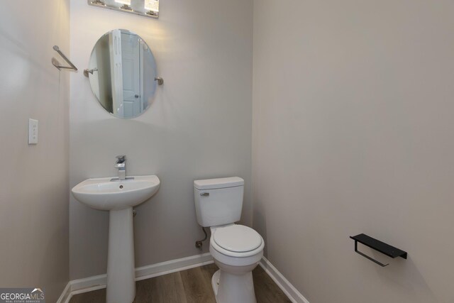 half bath featuring toilet, wood finished floors, baseboards, and a sink