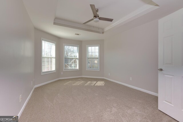 carpeted spare room with a raised ceiling, crown molding, baseboards, and ceiling fan