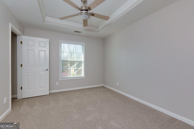 carpeted empty room with visible vents, crown molding, a raised ceiling, and baseboards