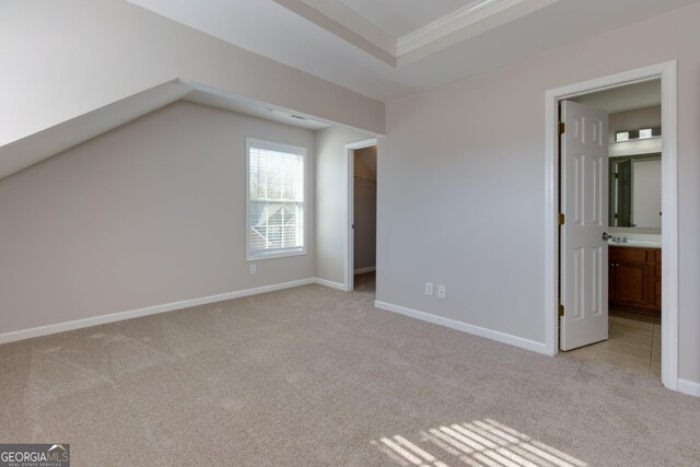 unfurnished bedroom featuring a tray ceiling, crown molding, baseboards, light colored carpet, and a spacious closet
