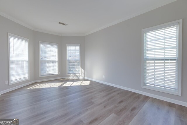 unfurnished room with visible vents, wood finished floors, baseboards, and ornamental molding