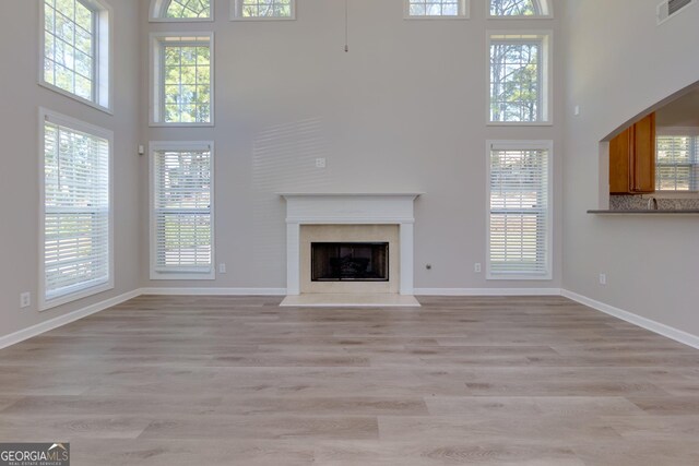 unfurnished living room with a high end fireplace, visible vents, baseboards, light wood-type flooring, and a high ceiling