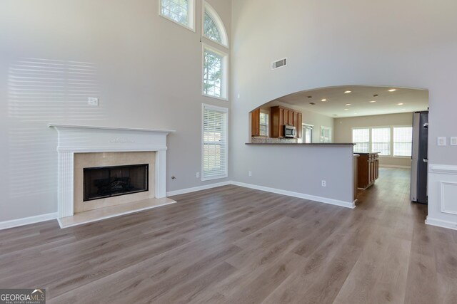 unfurnished living room with visible vents, a fireplace with raised hearth, baseboards, and wood finished floors