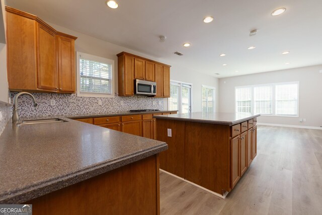kitchen with tasteful backsplash, stainless steel microwave, a center island, brown cabinets, and a sink