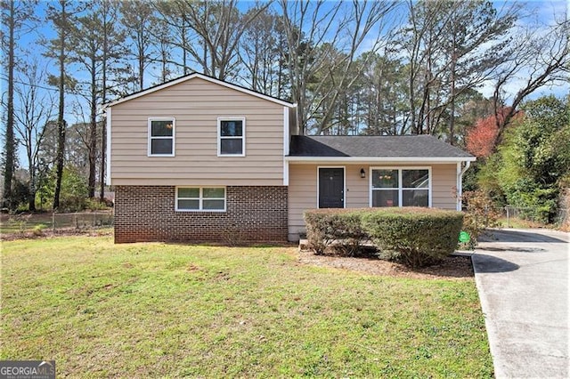 tri-level home with a front yard, concrete driveway, fence, and brick siding