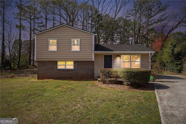 tri-level home with a front yard, concrete driveway, fence, and brick siding