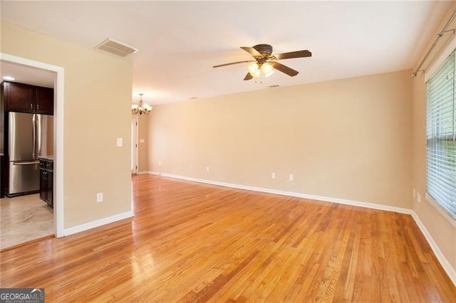 unfurnished room with visible vents, ceiling fan with notable chandelier, light wood-style floors, and baseboards