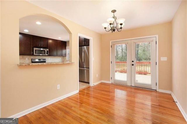 interior space featuring light wood-type flooring, french doors, arched walkways, baseboards, and a chandelier