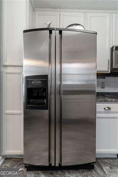 interior details featuring a textured ceiling, backsplash, stainless steel fridge with ice dispenser, and white cabinetry
