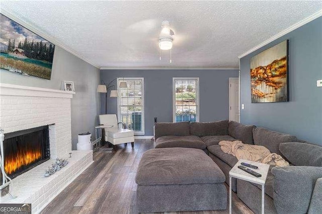 living room with ceiling fan, ornamental molding, a fireplace, wood finished floors, and a textured ceiling
