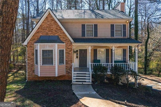 view of front facade featuring brick siding, covered porch, a chimney, and a shingled roof