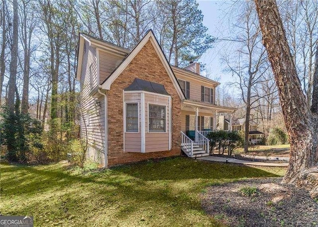 view of front facade with brick siding, covered porch, a chimney, and a front yard