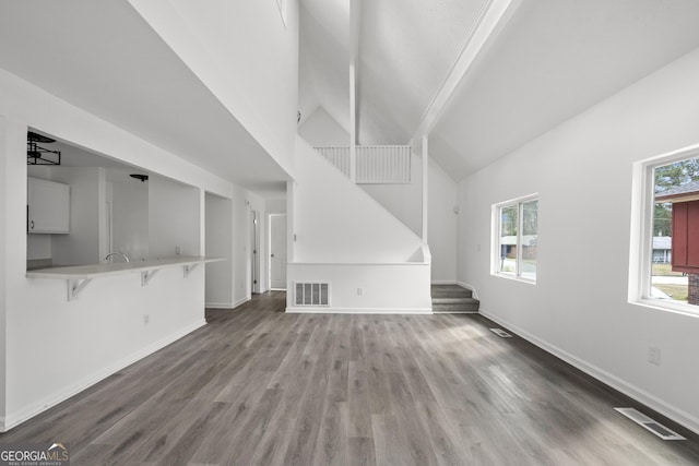 unfurnished living room with wood finished floors, baseboards, stairs, and visible vents