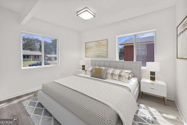bedroom with baseboards, wood finished floors, and beam ceiling